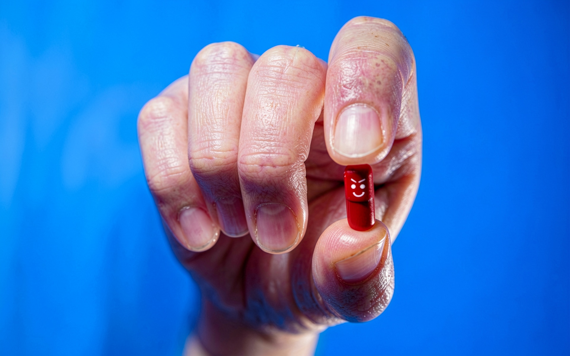 Красная капсула в пальцах на синем фоне