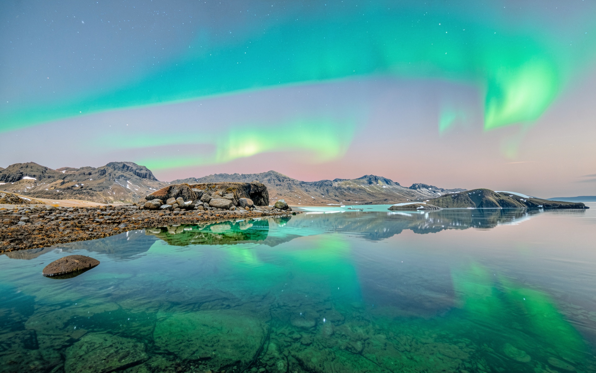 Северное сияние над скалистым берегом озера